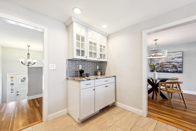 bar featuring white cabinetry, light stone counters, decorative light fixtures, a notable chandelier, and backsplash