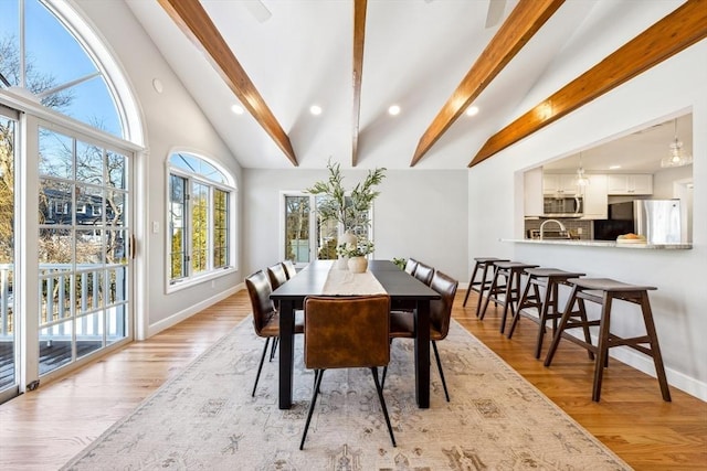 dining area featuring sink, beam ceiling, high vaulted ceiling, and light hardwood / wood-style flooring