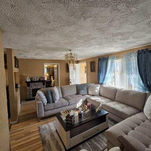 living area featuring a textured ceiling, a stone fireplace, and wood finished floors