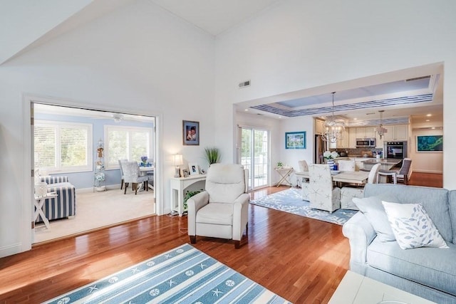 living room with a high ceiling, ceiling fan with notable chandelier, hardwood / wood-style flooring, and a tray ceiling