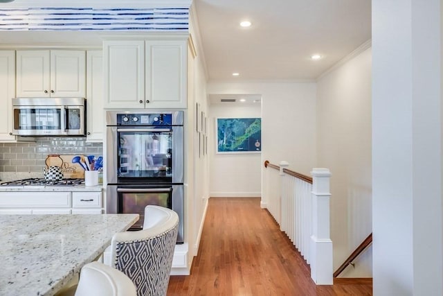 kitchen featuring light stone countertops, appliances with stainless steel finishes, decorative backsplash, white cabinets, and light hardwood / wood-style floors