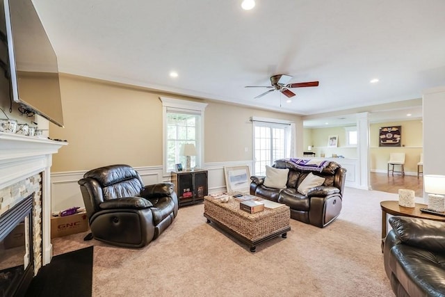 living room featuring light carpet, a stone fireplace, and ceiling fan