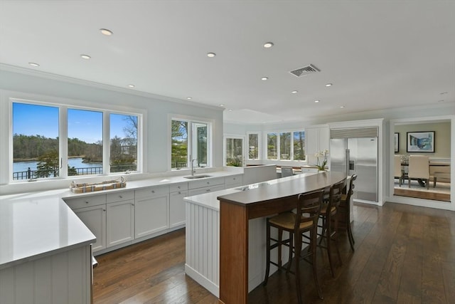kitchen with visible vents, stainless steel built in refrigerator, dark wood-style flooring, a sink, and a center island
