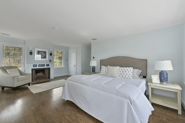 bedroom featuring a fireplace with flush hearth, wood finished floors, visible vents, and baseboards