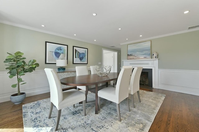 dining room with visible vents, a wainscoted wall, wood finished floors, a fireplace, and crown molding