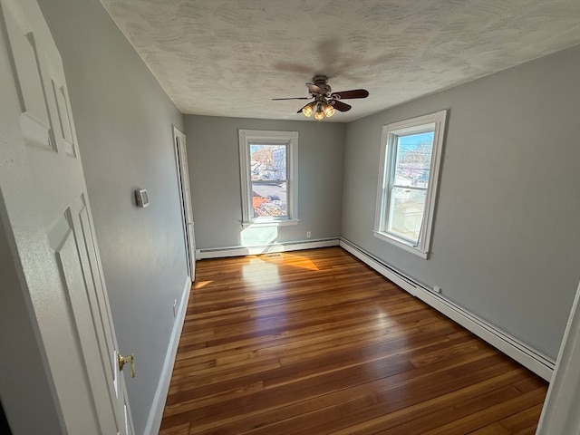 empty room featuring dark hardwood / wood-style floors, ceiling fan, and a baseboard heating unit