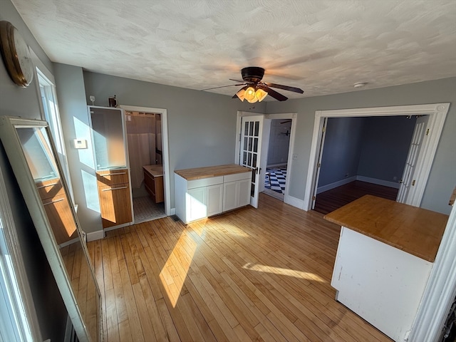 interior space featuring light wood-type flooring, a textured ceiling, ceiling fan, connected bathroom, and a closet