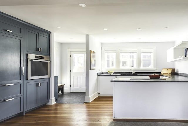 kitchen with dark wood-style flooring, a peninsula, dark countertops, stainless steel oven, and a sink
