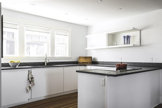 kitchen featuring open shelves, a sink, a peninsula, and dark countertops