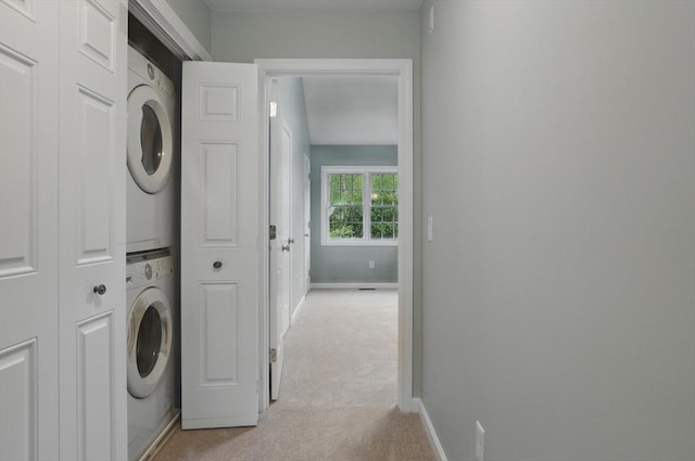 clothes washing area featuring stacked washer / dryer, light carpet, and baseboards