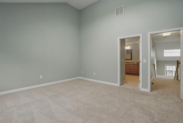 unfurnished bedroom featuring light colored carpet, baseboards, high vaulted ceiling, and ensuite bath