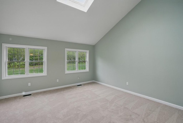 empty room featuring a skylight, baseboards, light carpet, and lofted ceiling