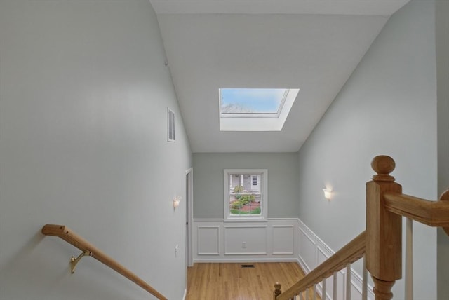 stairs with a skylight, wood finished floors, and a wainscoted wall