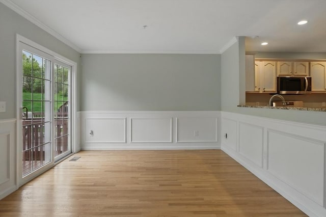 unfurnished dining area featuring crown molding, light wood-style flooring, a wainscoted wall, recessed lighting, and a sink