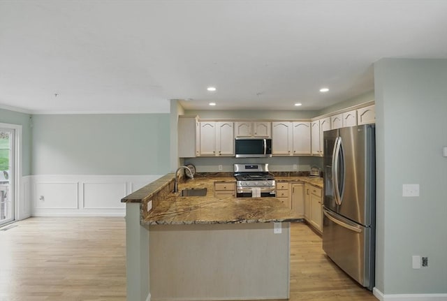 kitchen with stainless steel appliances, a peninsula, a sink, dark stone countertops, and light wood-type flooring