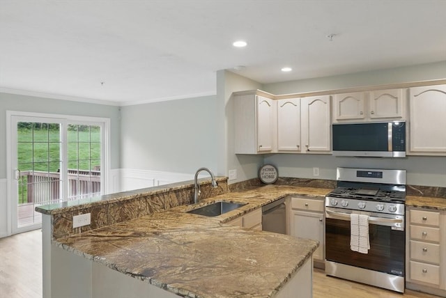 kitchen featuring stainless steel appliances, a sink, a peninsula, ornamental molding, and light wood finished floors