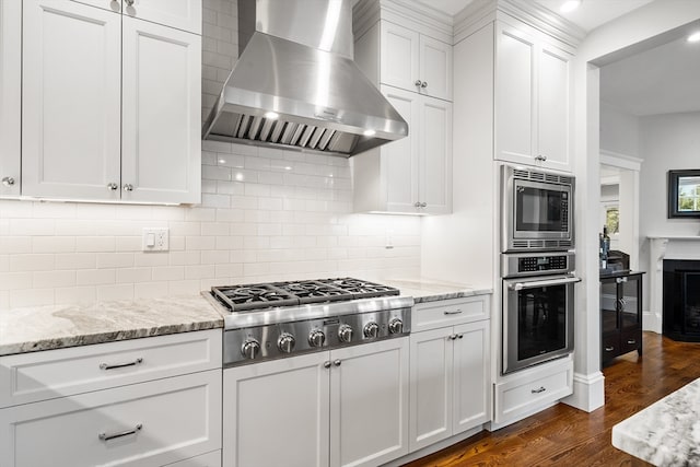 kitchen with white cabinets, wall chimney exhaust hood, stainless steel appliances, dark hardwood / wood-style floors, and decorative backsplash