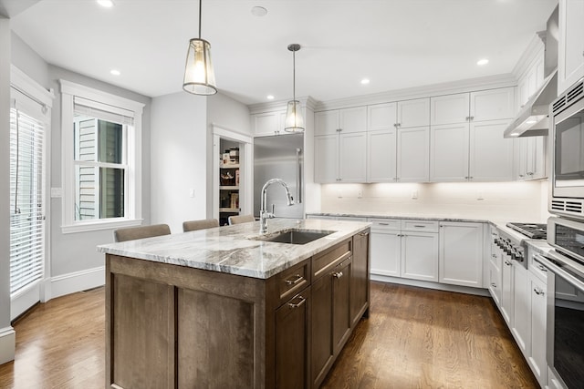 kitchen with pendant lighting, dark wood-type flooring, sink, an island with sink, and white cabinets