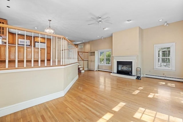 unfurnished living room with wood finished floors, baseboards, baseboard heating, stairway, and ceiling fan with notable chandelier