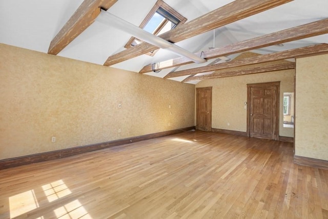 spare room featuring baseboards, lofted ceiling with beams, a healthy amount of sunlight, and light wood-style flooring