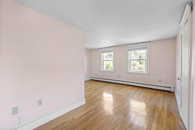 empty room featuring baseboards, light wood-style floors, and baseboard heating