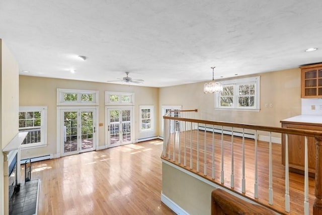 interior space featuring baseboards, baseboard heating, ceiling fan with notable chandelier, and light wood-type flooring