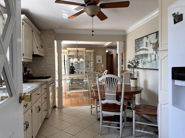 dining room featuring light tile patterned floors, ornamental molding, ceiling fan with notable chandelier, and ornate columns