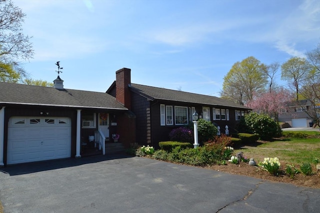 ranch-style house with a garage, roof with shingles, a chimney, and aphalt driveway