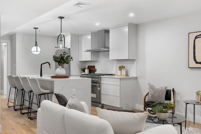 kitchen featuring light wood-type flooring, stainless steel appliances, sink, wall chimney range hood, and pendant lighting