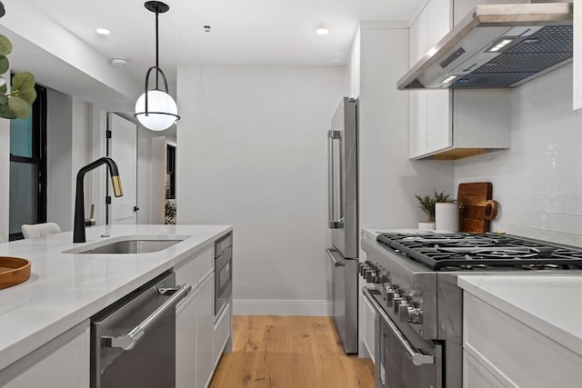 kitchen with light stone countertops, premium appliances, wall chimney range hood, white cabinets, and hanging light fixtures