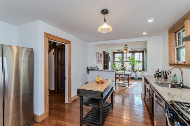 kitchen with light stone counters, tasteful backsplash, a sink, appliances with stainless steel finishes, and wood finished floors