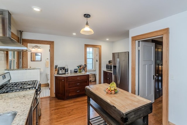 kitchen featuring dark brown cabinetry, decorative backsplash, appliances with stainless steel finishes, light wood-type flooring, and wall chimney exhaust hood