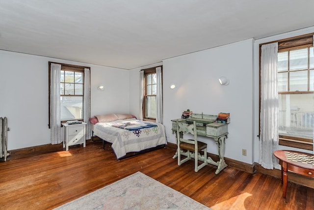 bedroom featuring baseboards, radiator, wood finished floors, and multiple windows