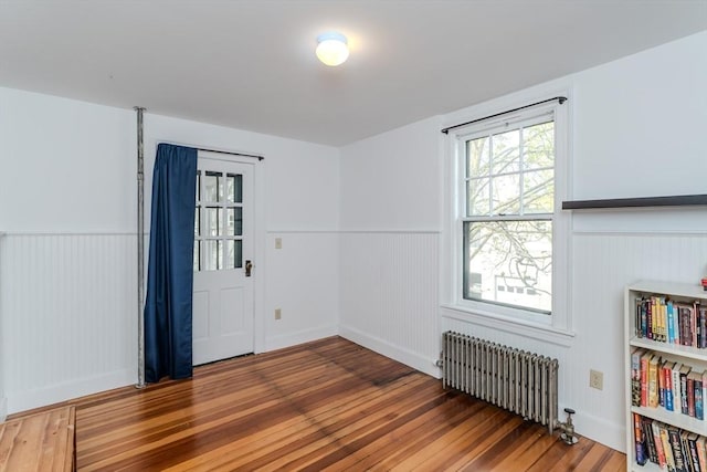 empty room featuring radiator heating unit, wood finished floors, wainscoting, and a decorative wall