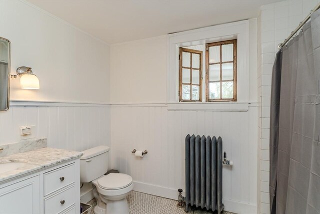 bathroom with toilet, radiator heating unit, vanity, and a wainscoted wall