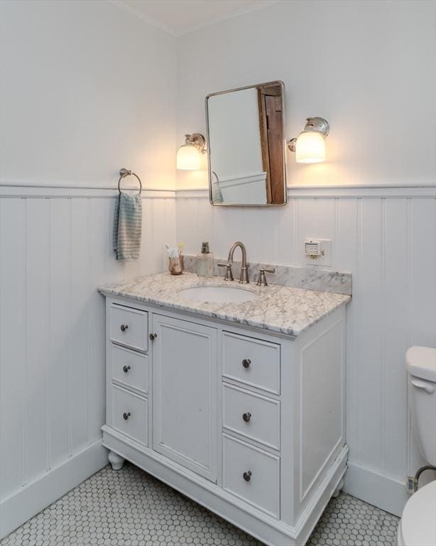 bathroom featuring a decorative wall, toilet, tile patterned flooring, and wainscoting