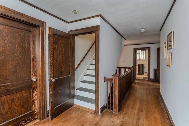 corridor featuring crown molding, stairway, baseboards, radiator, and wood finished floors