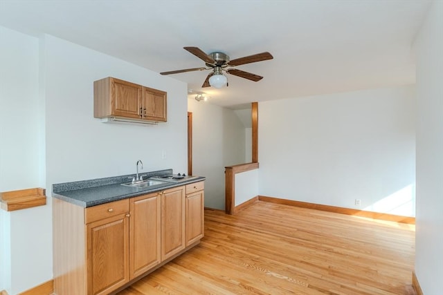 kitchen with dark countertops, ceiling fan, a sink, baseboards, and light wood-type flooring