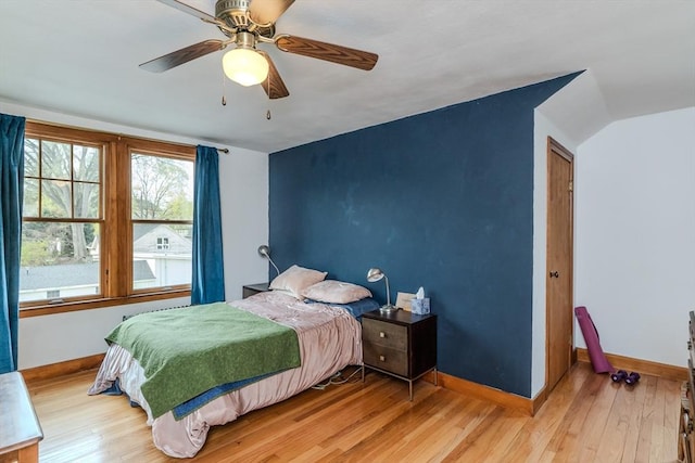 bedroom with light wood-type flooring, a ceiling fan, vaulted ceiling, and baseboards