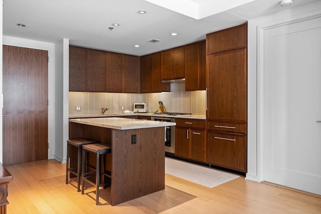 580 Washington St Unit 411, Boston, MA 02111 - kitchen with a breakfast bar area, tasteful backsplash, a kitchen island, and light wood-style flooring