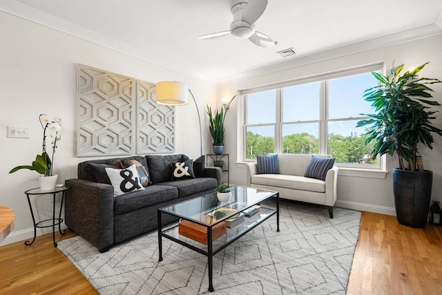 living room with ornamental molding, healthy amount of natural light, light wood finished floors, baseboards, and ceiling fan