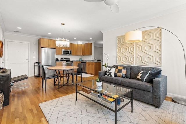 living room featuring light wood-type flooring, ornamental molding, recessed lighting, baseboards, and a chandelier