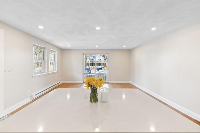 interior space with baseboards, a baseboard heating unit, wood finished floors, and recessed lighting