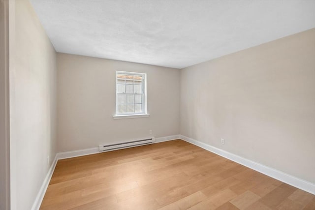 empty room with a baseboard heating unit, light wood-type flooring, and baseboards