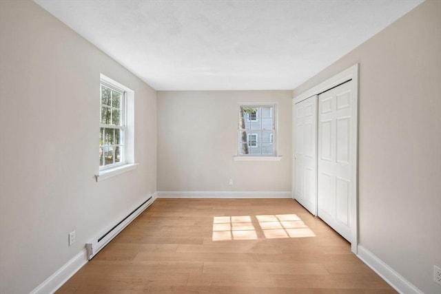 unfurnished bedroom featuring a baseboard heating unit, light wood-type flooring, a closet, and baseboards