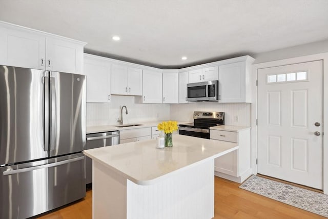 kitchen featuring a sink, a kitchen island, white cabinetry, light countertops, and appliances with stainless steel finishes