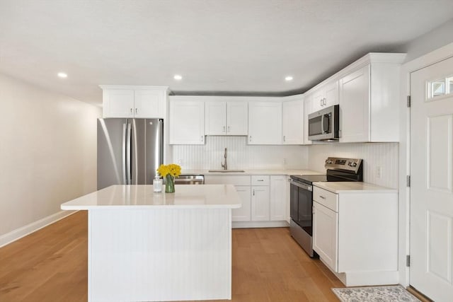 kitchen with light wood finished floors, a kitchen island, stainless steel appliances, white cabinetry, and a sink