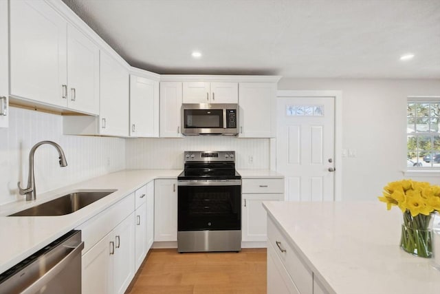 kitchen featuring white cabinets, appliances with stainless steel finishes, light countertops, light wood-type flooring, and a sink