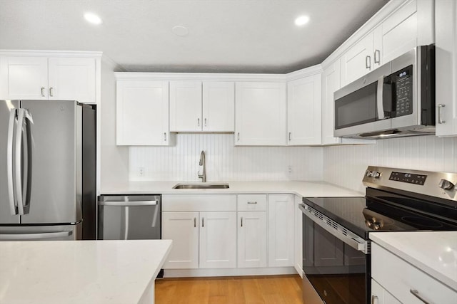 kitchen featuring stainless steel appliances, light countertops, light wood-type flooring, white cabinetry, and a sink