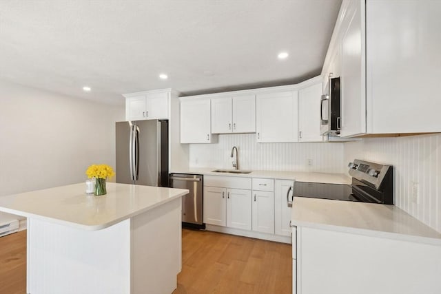 kitchen with light wood finished floors, stainless steel appliances, light countertops, white cabinets, and a sink